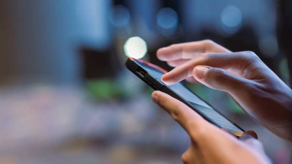 A person holding a mobile phone in one hand and tapping the screen with the other hand.
