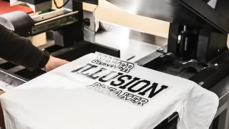 A person is preparing to print “Maker Illusion Breaker” text on a white t-shirt.