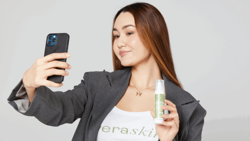 A young woman filming herself while presenting a product as a giveaway back-to-school marketing activity.