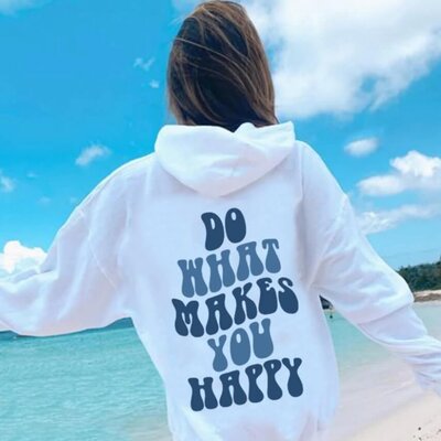 A woman on a beach wearing a white hoodie that says"Do what makes you happy."