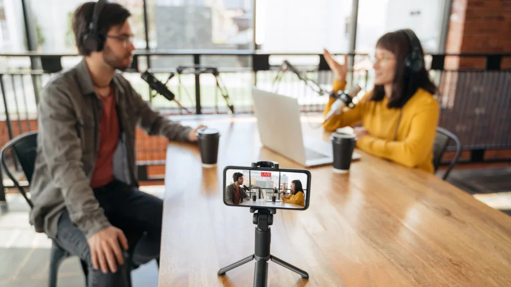 A man and woman at a table, both recording a video podcast for their YouTube channel.