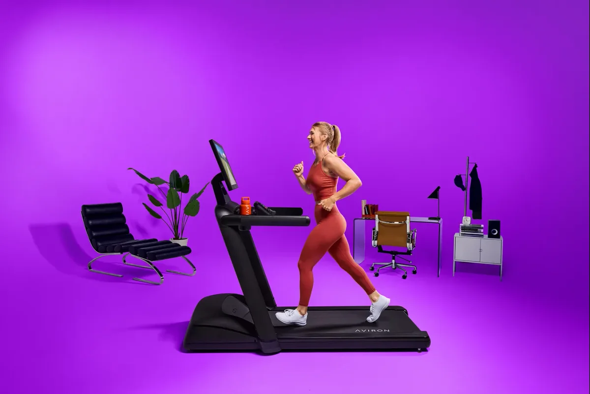 Woman enjoying a running workout on an Aviron Victory Treadmill against a purple background