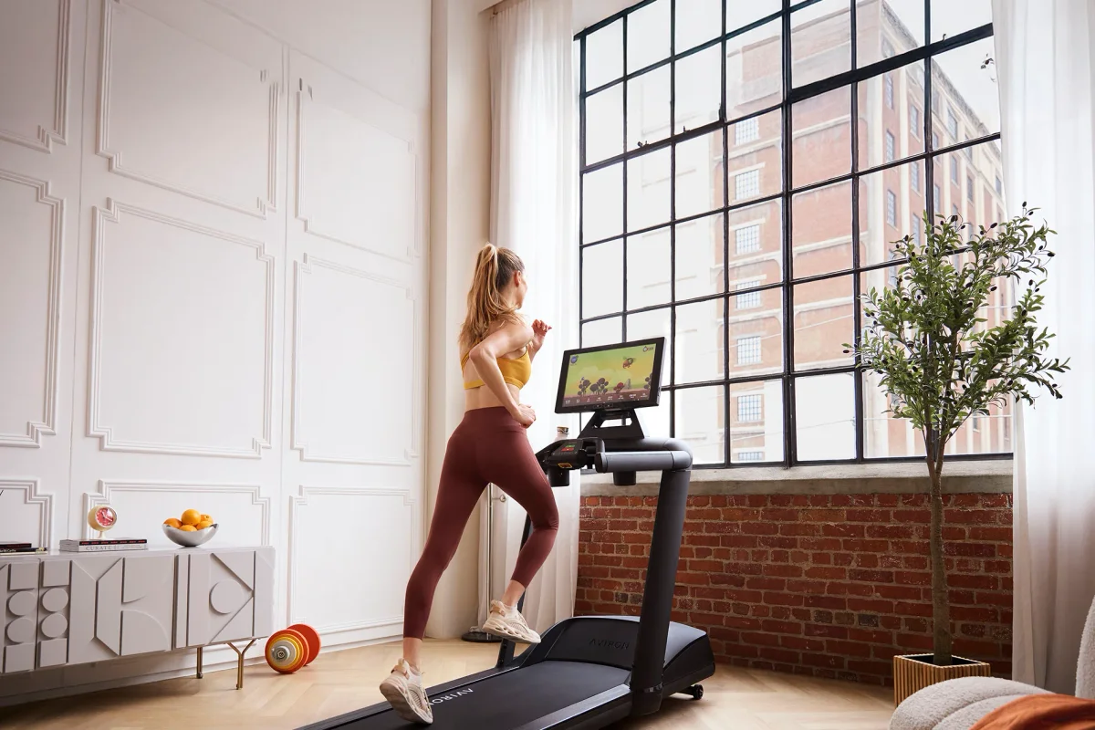 Woman doing a short treadmill workout at home on an Aviron Victory Treadmill with a game on the screen