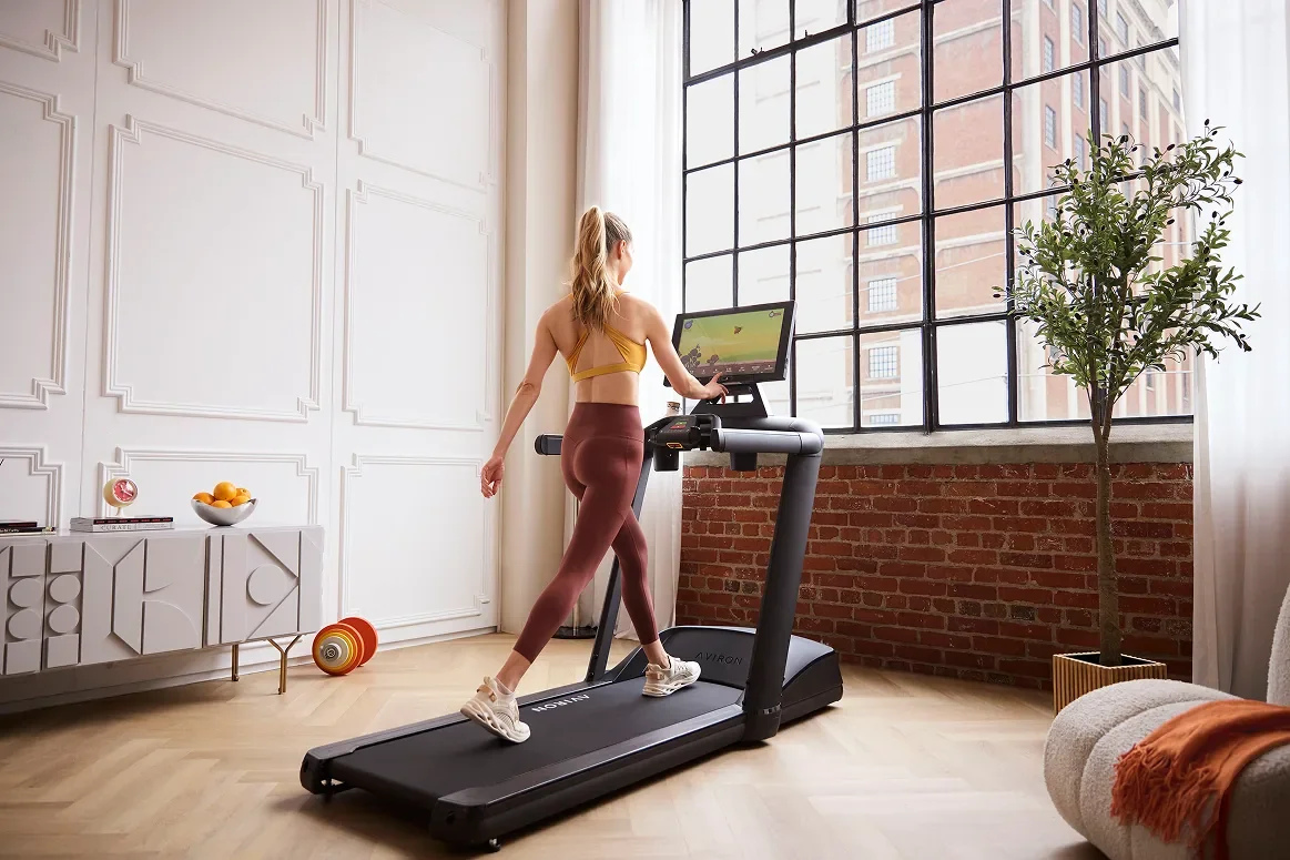 Woman doing an incline walking workout on an Aviron Victory Treadmill in a bright home loft