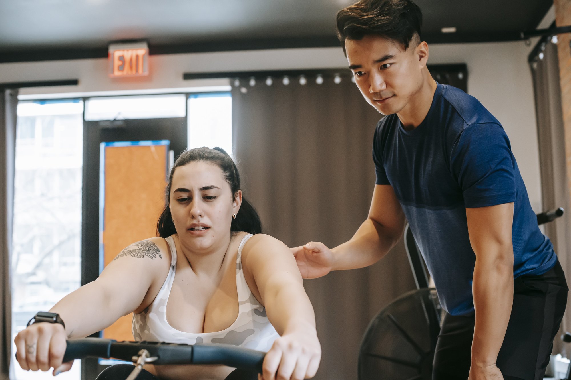 Trainer coaching a rower on back position during rowing machine form practice.