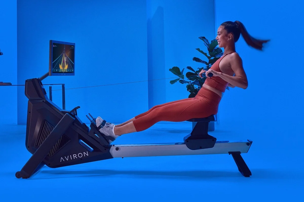 Woman rowing on an Aviron rower with a neon racing game on the touchscreen