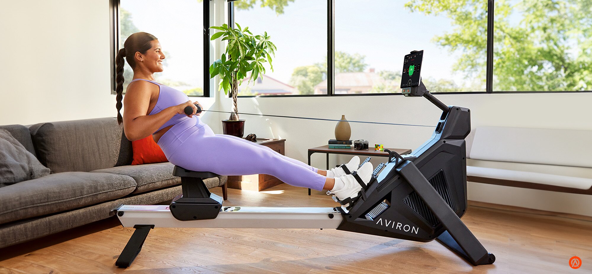 Person rowing indoors on an Aviron rowing machine in a bright home workout space.