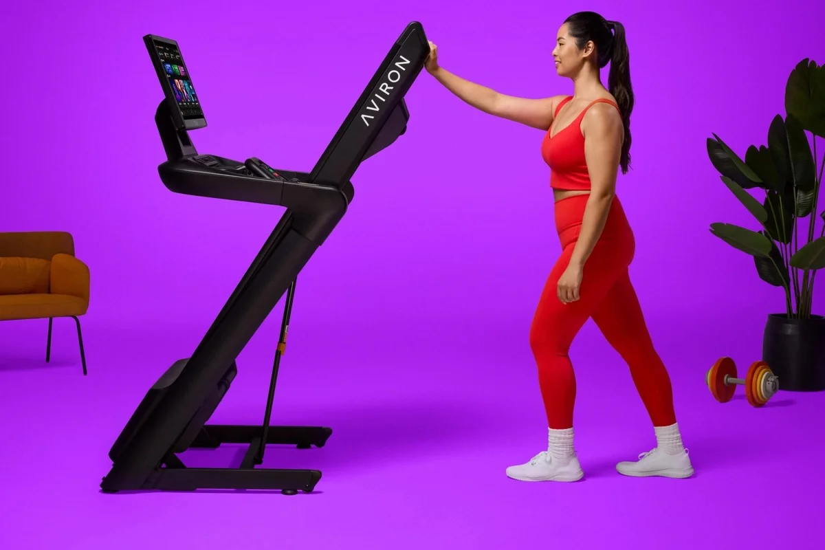 Woman folding the Aviron Justice treadmill upright with one hand using the SafeLift pneumatic assist
