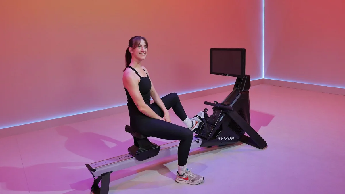 Rower sitting at the catch position on an Aviron Strong Rower with the monitor visible, ready to check split and stroke rate