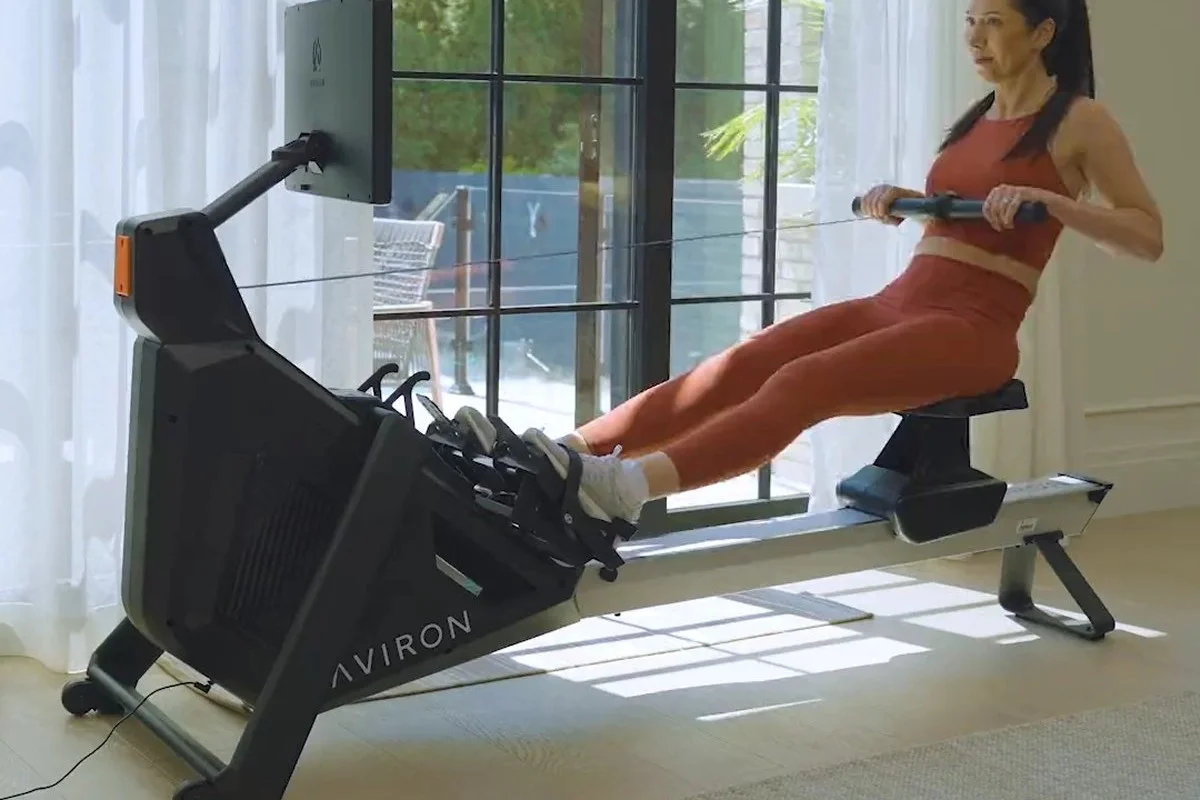 Woman rowing on the Aviron Strong Series Rower in a bright living room by tall windows