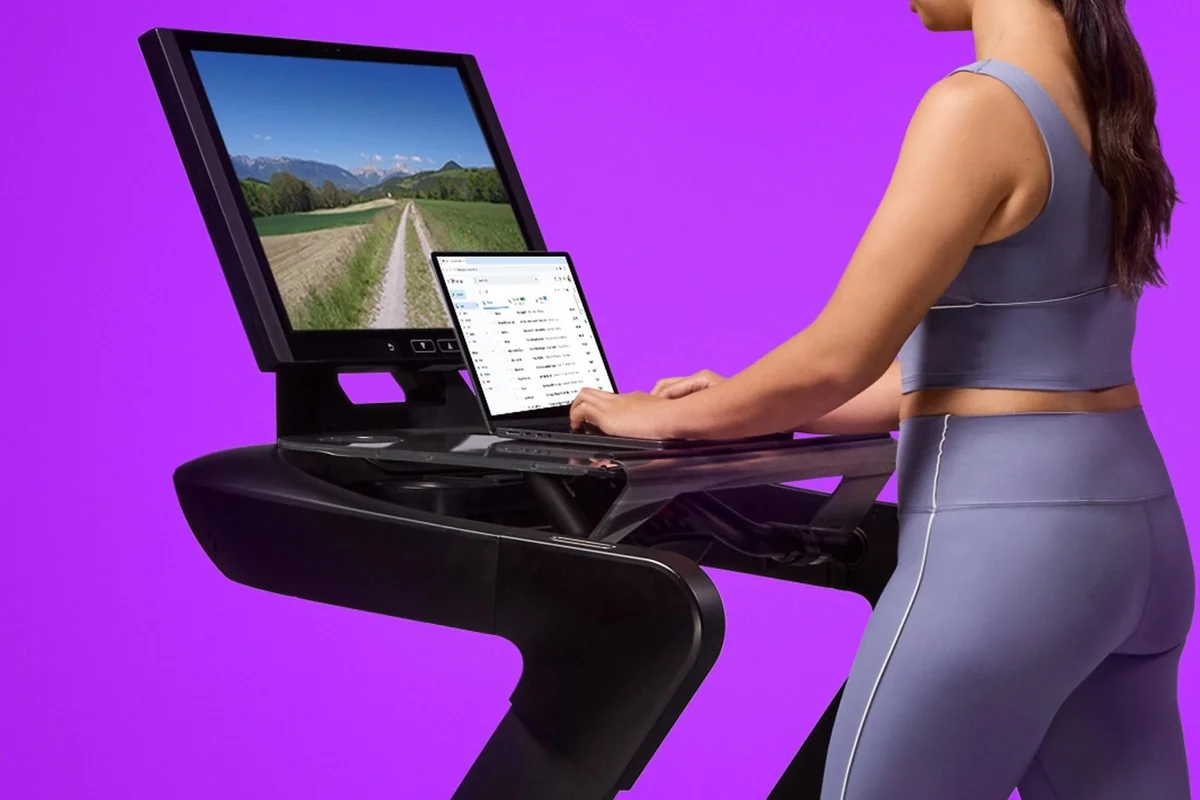 Woman walking and typing on a laptop at the Aviron WalkDesk, with a scenic route on the treadmill screen