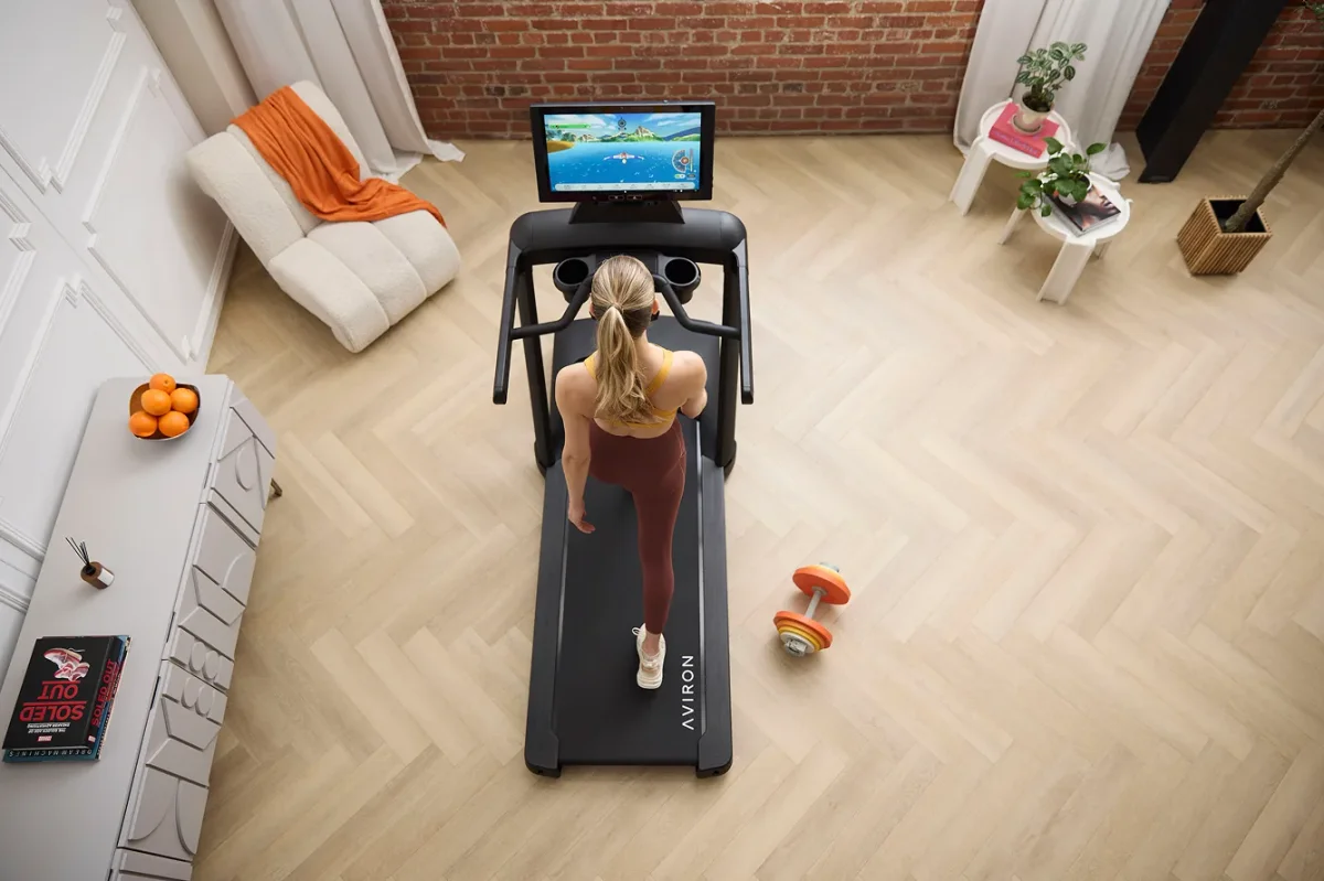 Overhead view of a woman running on an Aviron Victory treadmill with a scenic game on the screen