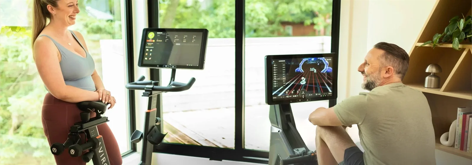 Couple at home, the man rowing on an Aviron Strong Series Rower with a lane-racing game and leaderboard on the screen