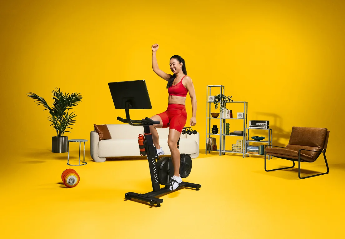 Woman celebrating during a beginner stationary bike workout on an Aviron Fit Bike S at home