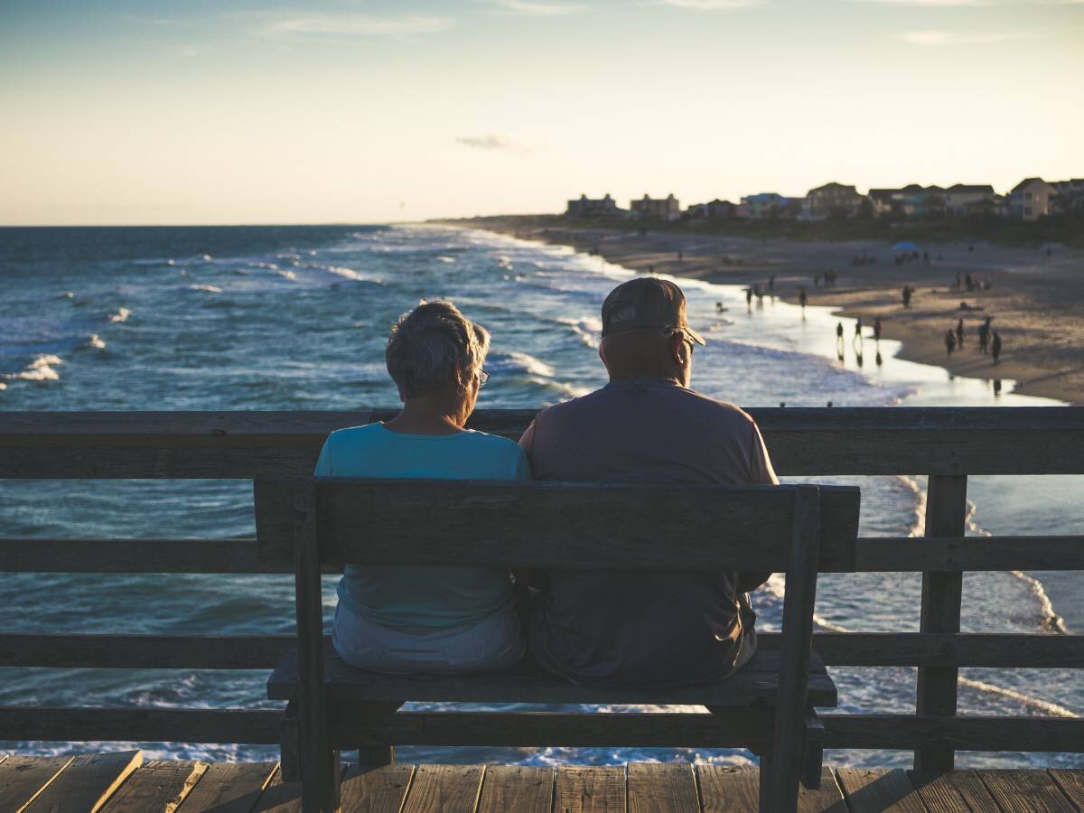 65 year old couple enjoying the sunset on a bench at the beach