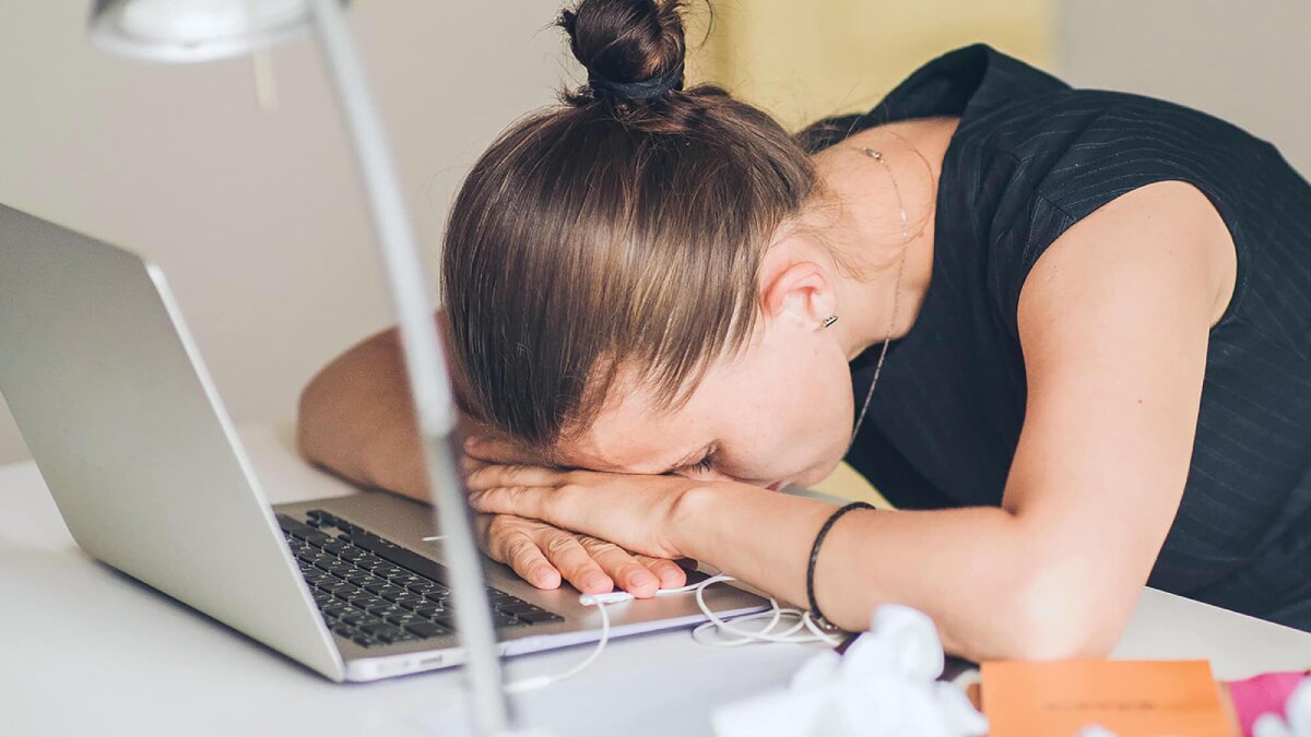 A woman with her head resting on the computer, showing signs of exhaustion or stress.