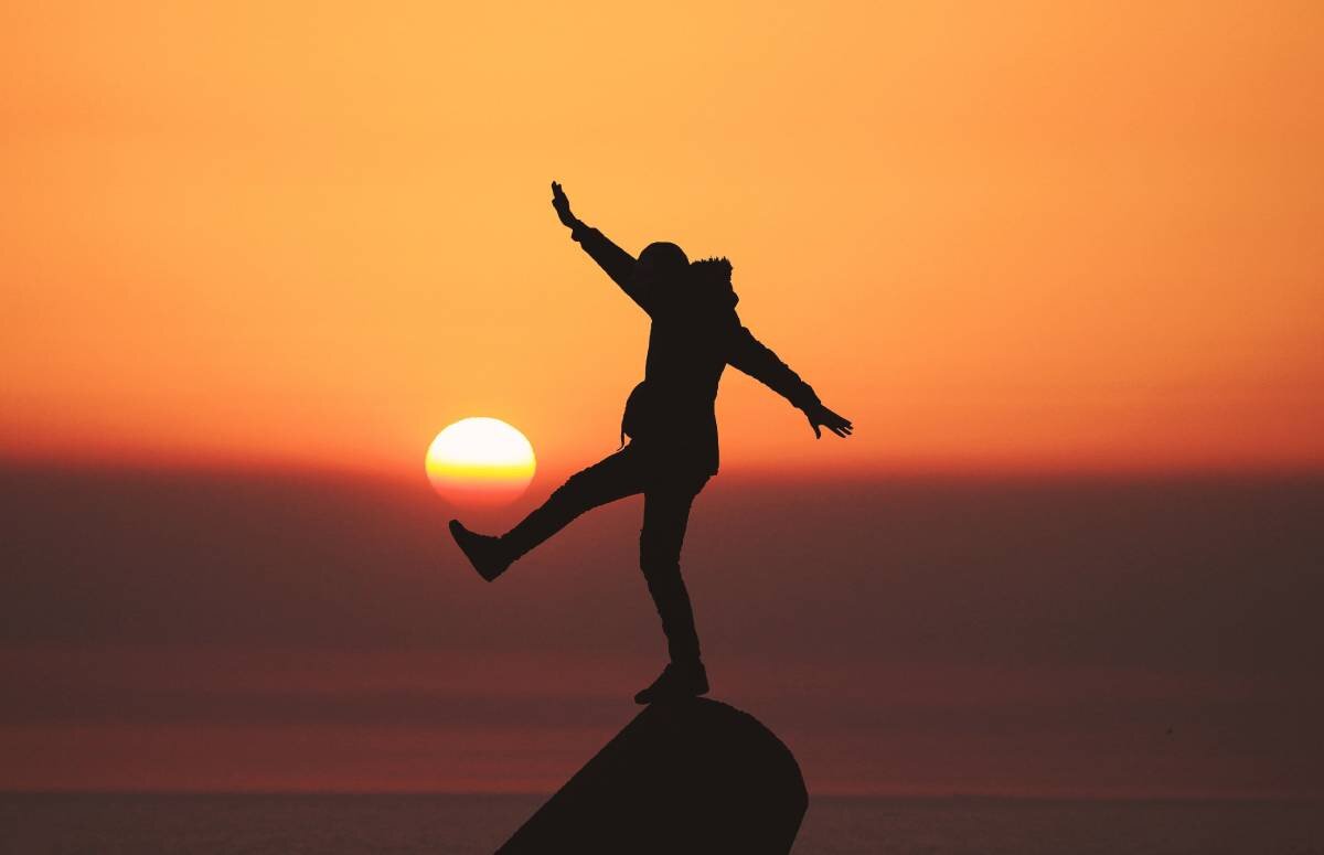 Person balancing on a stone at sunset