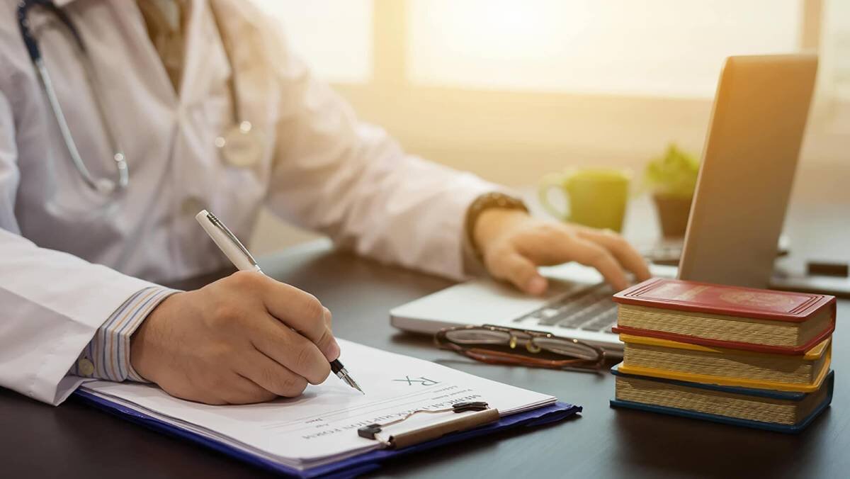 Doctor writing a prescription while using a computer