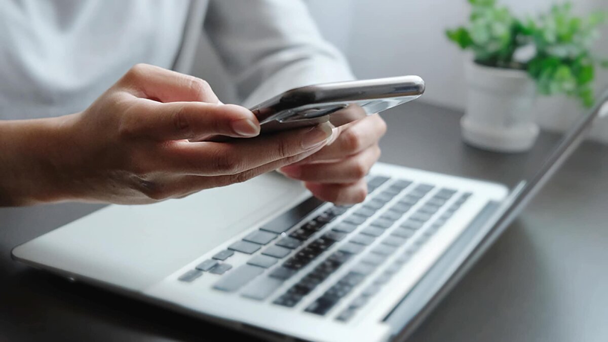 A person sitting at a table with a laptop, using their cellphone