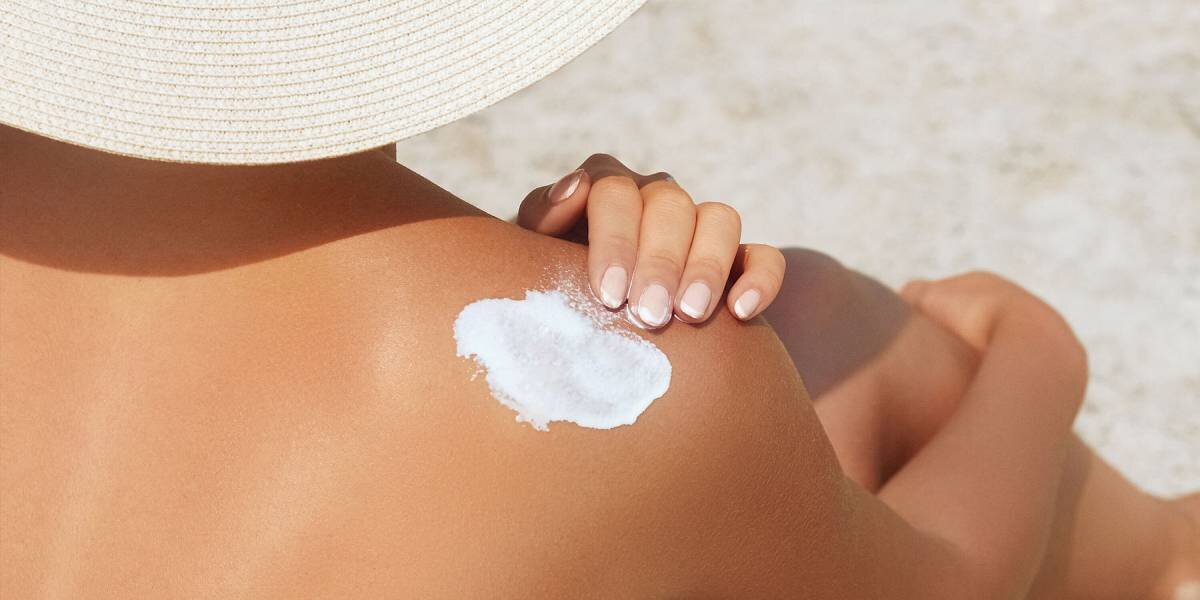 Woman applying sunscreen on behind her shoulder
