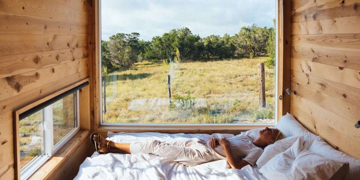 A woman is resting on a bed next to a window.