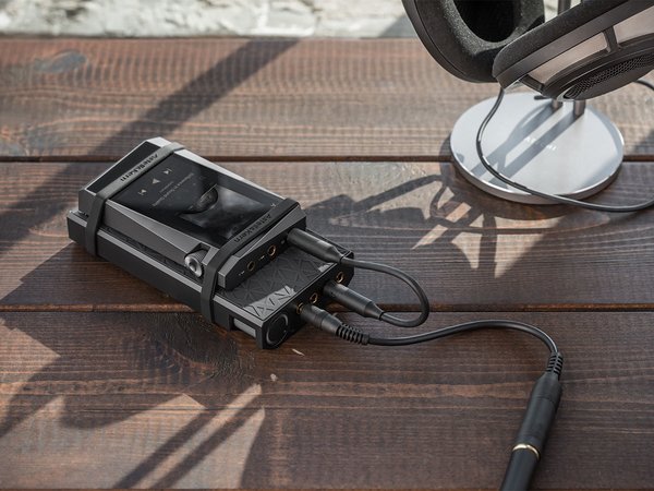 Astell&Kern PA10 Amp rubber banded to a music player and sitting on a table next to a headphone stand.