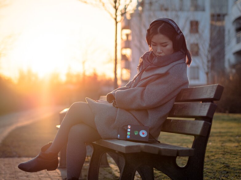 woman on a bench outside listening to headphones with Hugo 2 next to her