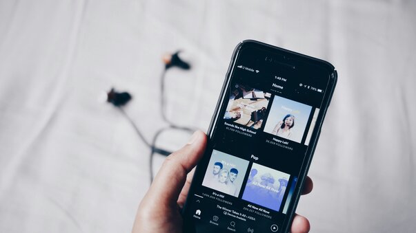 Person holding phone with earbuds in background and streaming app open