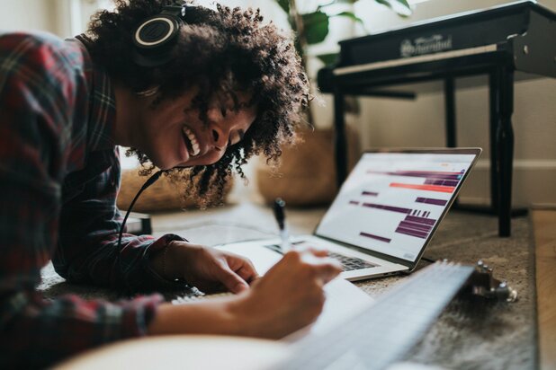 Woman writing on a piece of paper while wearing headphones 