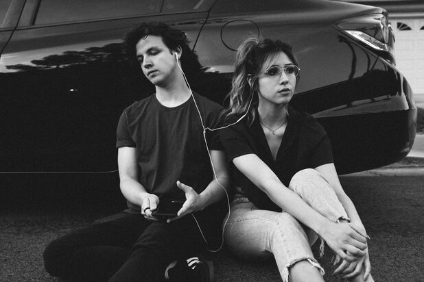Man and woman sitting next to each other sharing a pair of earbuds with one earbud in each ear