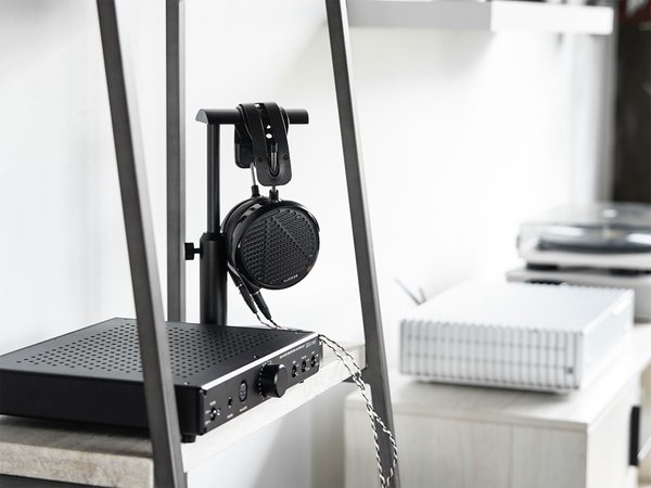 HeadAmp GS-X mini amp sitting on a shelf with headphones hanging from a stand beside it.