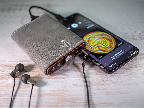iFi Hip DAC 2 lifestyle shot in a leather case with a music player and IEMs on a table