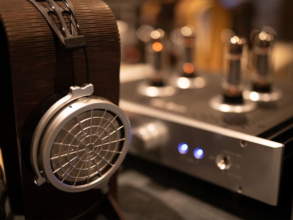 A closeup shot of the Blue Hawaii by HeadAmp next to a pair of headphones sitting on a stand. 