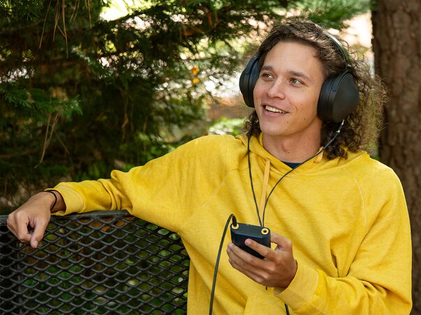 Man wearing Sony headphones holding a Digital Audio Player sitting on a bench 
