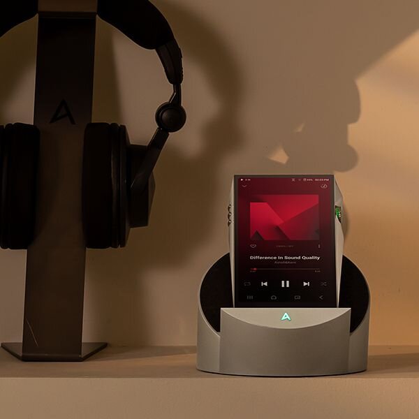 PD10 on the docking cradle on a table next to the headphones on a stand