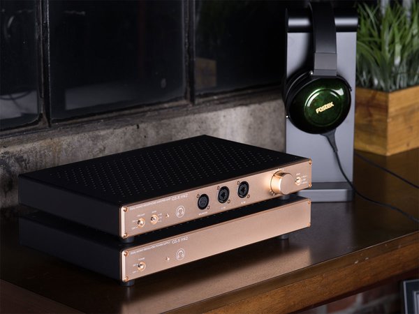 HeadAmp's GS-X Mk2 Amplifier sitting on a table next to headphones hanging from a stand.