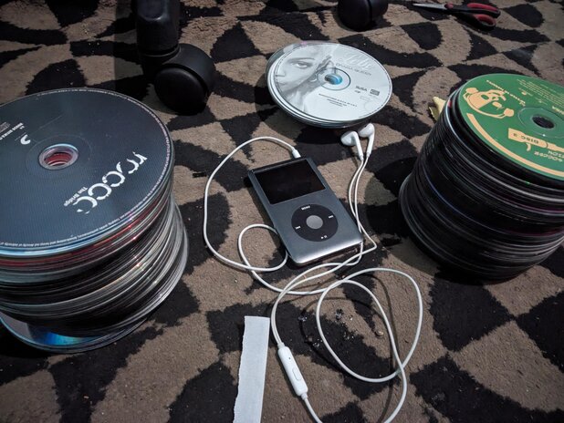 Apple iPod with wired earphones attached and CD stacks next to 