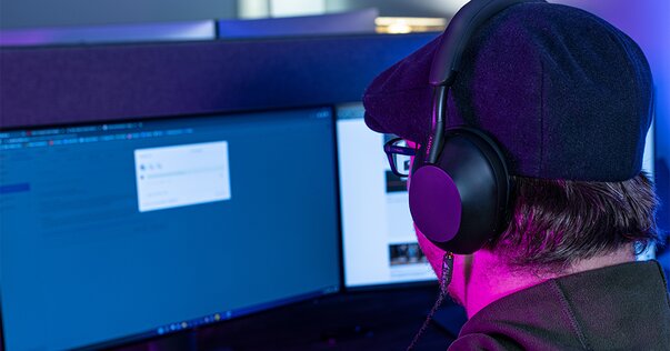 man wearing sony wireless headphones looking at two computer screens