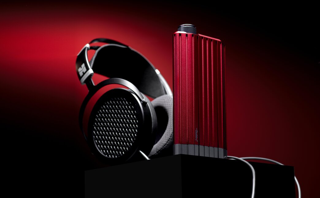 iFi iDSD Diablo 2 with HiFiMan headphones tilted behind the DAC with a red background