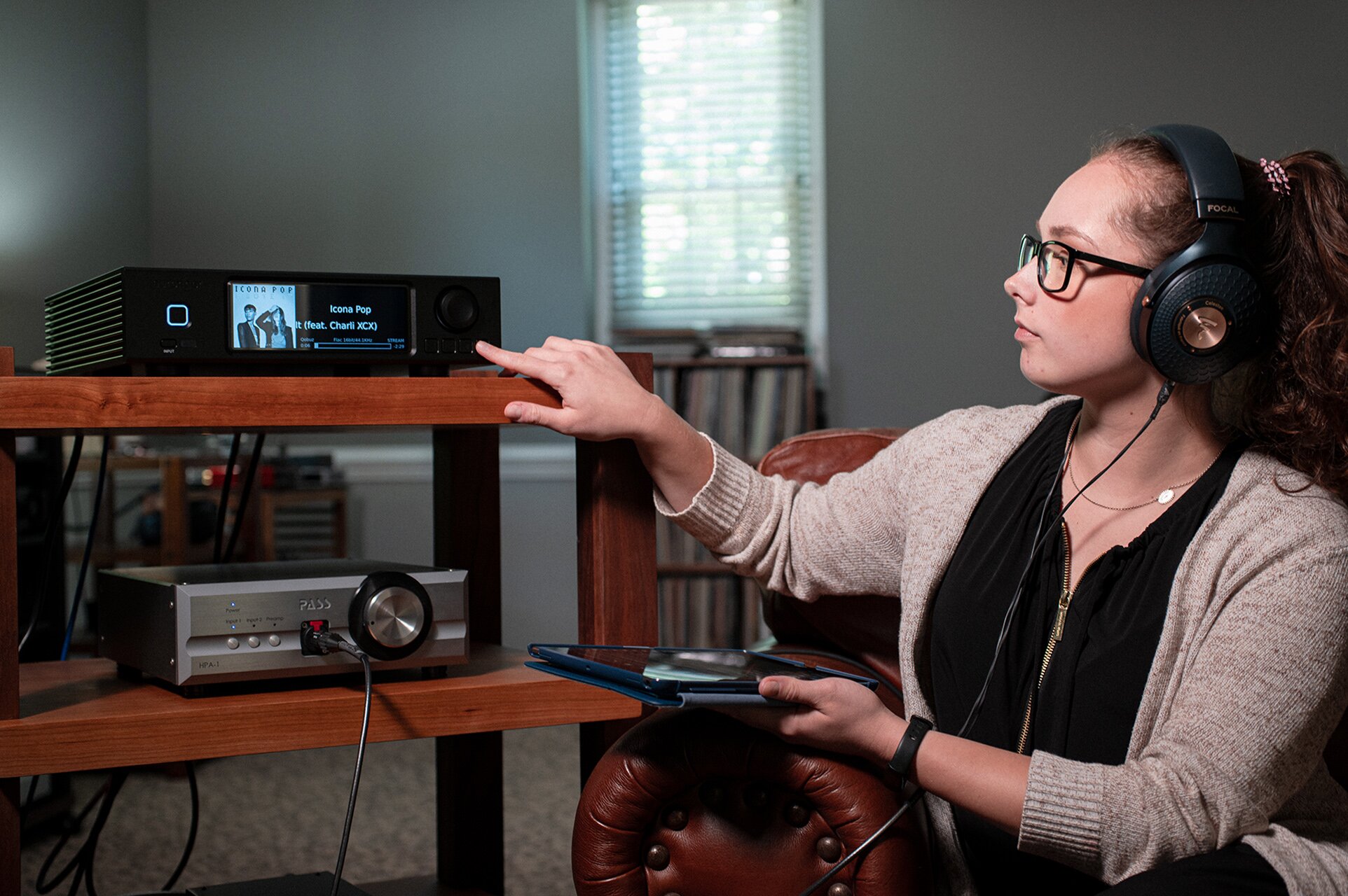 Woman wearing headphones holding an Apple iPad in one hand and touching the Aurender A200 Music Streamer with the other hand