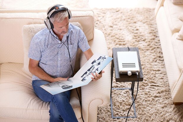 Man sitting on couch wearing the Warwick Acoustics BRAVURA Headphones connected to the BRAVURA Headphone Amplifier