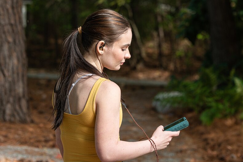 Girl walking and carrying a music player while listening to IEMs