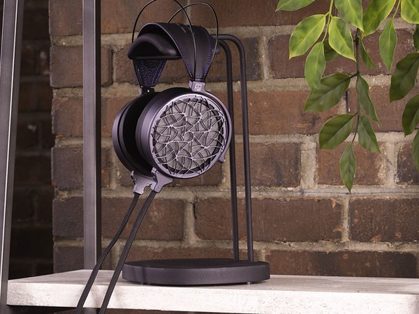 COINA Electrostatic Headphones by Dan Clark Audio, hanging from a stand on a shelf next to a plant.