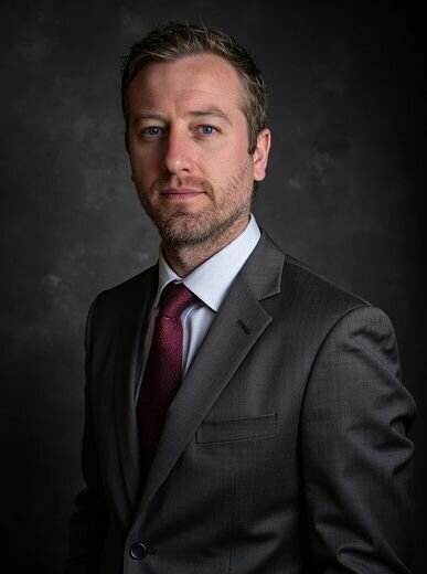 AI portrait of a serious man in a charcoal gray suit and burgundy tie, set against a dramatic studio backdrop—Somny’s corporate executive headshot style.