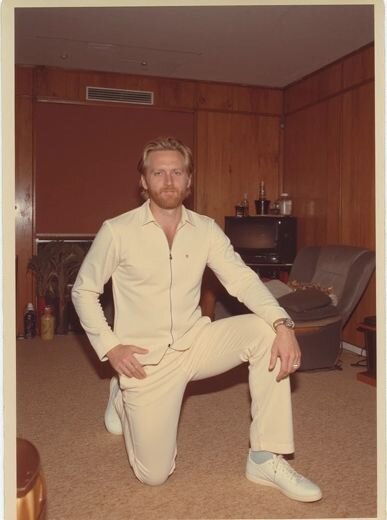 AI-generated image of a man in a cream leisure suit, posing in a 1970s wood-paneled room with relaxed swagger.