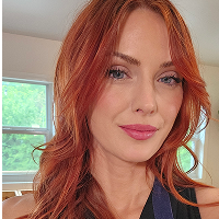 Portrait of the same woman with red hair in casual clothing and natural indoor lighting.