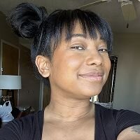 Photo of the same woman with black hair in a top bun, smiling in a casual indoor setting.