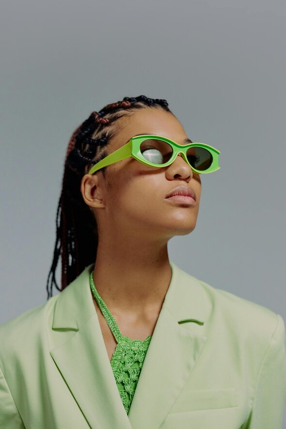 The CSRD: A Game Changer for Fashion Transparency. Woman looks of into the distance wearing green sunglasses and a green blazer. 