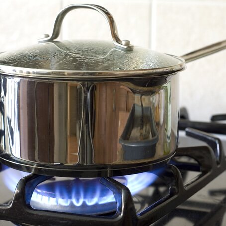 stainless steel pot with lid over an active natural gas stove