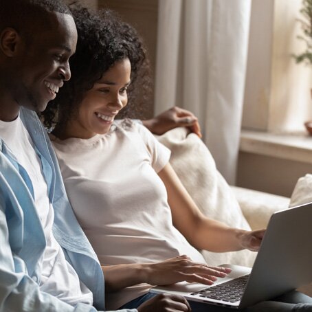 young man and woman sitting on couch looking at a laptop together